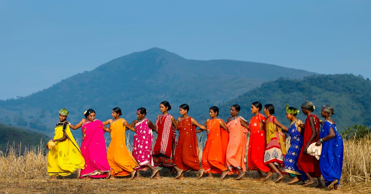 A group of women perform a traditional tribal dance in vibrant clothing against a rural Indian backdrop.