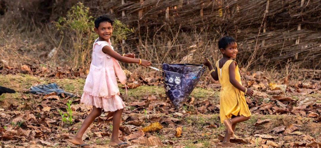Two children playing joyfully with a kite in an Indian village setting.