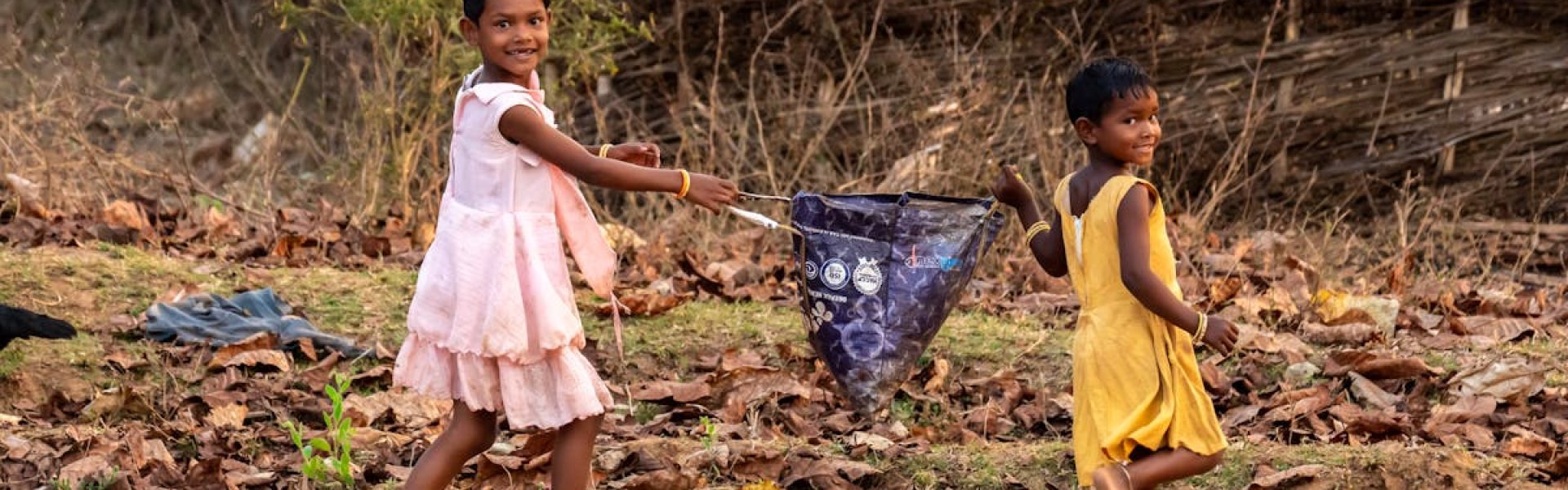 Two children playing joyfully with a kite in an Indian village setting.
